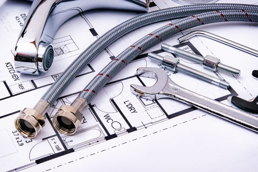 Plumbing tools and a faucet laid on a building blueprint