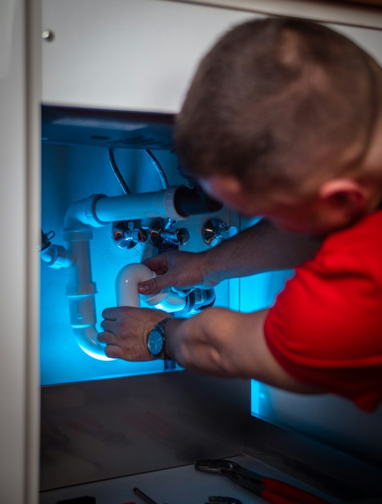 Technician repairing a leaking pipe inside a sink cabinet