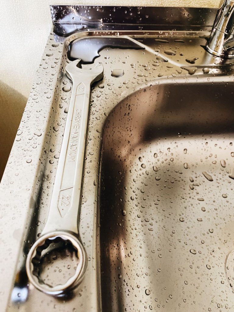 Wrench resting on a wet stainless steel kitchen sink